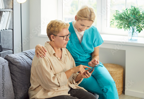Quadro su tela Kind caregiver nurse, senior woman sitting on sofa in home, older patient pointi