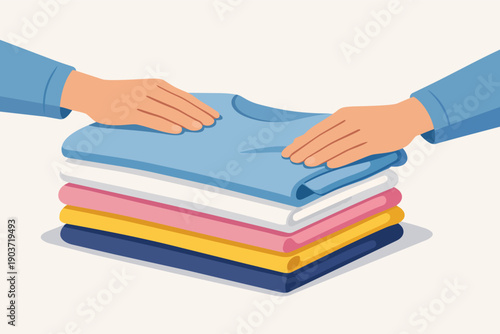 Hands folding clean clothes, placing top shirt on neatly stacked laundry pile