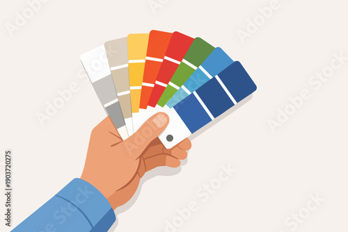 Hand holding a fan deck with various paint swatches, choosing colors for design projects