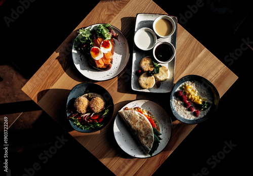 Overhead view of five different restaurant dishes arranged on a wooden table, showcasing a variety of gourmet meals. Perfect for menu or food photography.