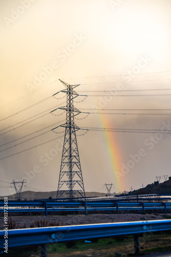 A rainbow appears over a power line tower
