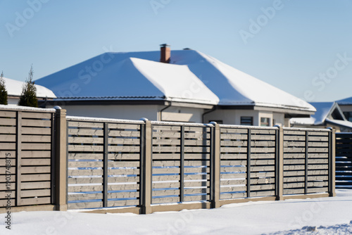 Residential house behind long horizontal timber fence, clean architecture and snowy yard, home security concept with private outdoor space and walkway