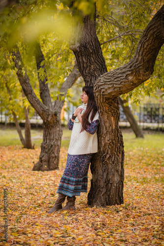 Autumnal thoughtfulness, a moment of reflection: a woman in a white sweater in a park by a tree with a book