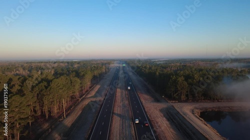 Drone flyover of open highway surrounded by forest and morning fog for travel and vacation themes