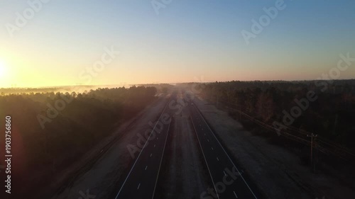 Aerial drone footage of scenic highway stretching through forest at sunrise during Florida road trip travel
