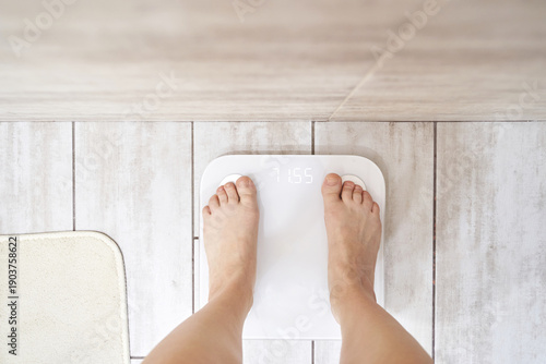 Female adult weighing on digital scale in bathroom for weight management and health tracking.