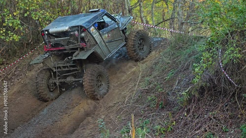 Extreme off-road competition with a custom 4x4 buggy climbing a difficult, muddy hill. The powerful vehicle navigates challenging terrain in a forest setting. Slow motion