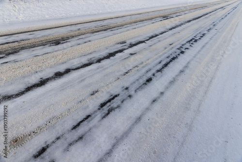 a close-up of an asphalt road with car ruts and part of the road completely covered with ice and snow, part of the road for cars in snow and ice after snowfalls and road treatment with salt