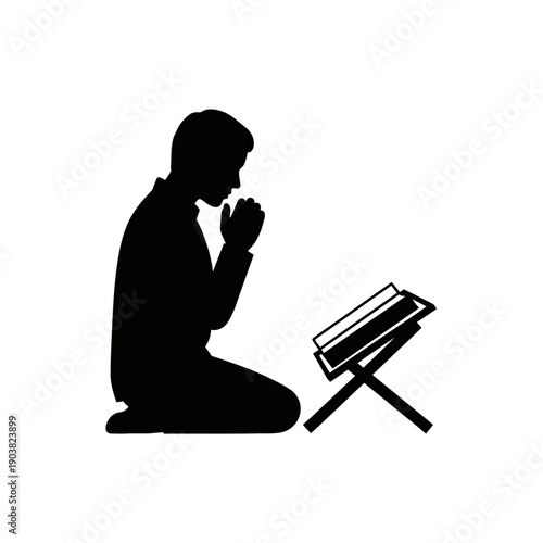 Silhouette of a man kneeling in prayer with an open book nearby