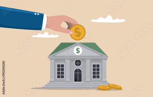 Hand putting a gold coin into a bank building representing savings and investment.