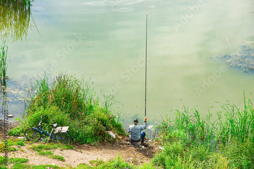 Fotografie A man is fishing by the edge of a murky lake