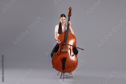 Foto Girl playing double bass on grey background