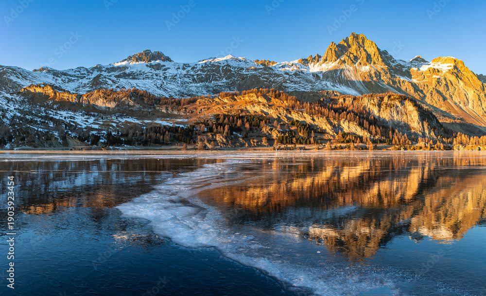 Obraz premium Sunset over the Alps mountain with reflection on the frozen lake with curvy opaque ice line on the Silsersee Lake in St. Moritz, Grisons, Switzerland