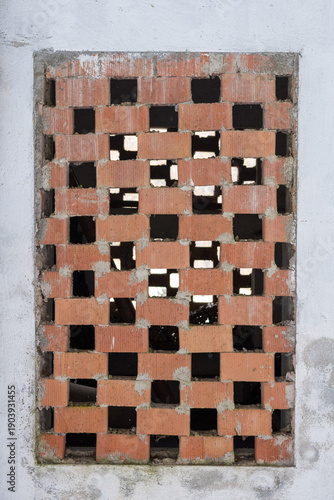 Traditional brick ventilation grid on an old farmhouse wall. Close up of a rustic geometric pattern made of red bricks in a rural Italian building, typical architecture of Northern Italy on mountain.