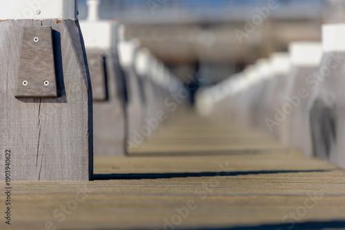 Selective focus lines of wooden poles of pier along the canal or river, Platform on pillars projecting from the shore or cost into the water, Sidewalk way by haven, quay shore or harbor, Netherlands.