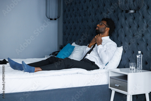 Young black entrepreneur loosen one's tie lying on comfortable bed