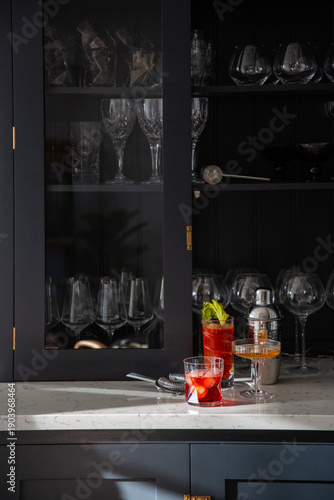 Dresser containing stemware with mixed drinks and a cocktail shaker.