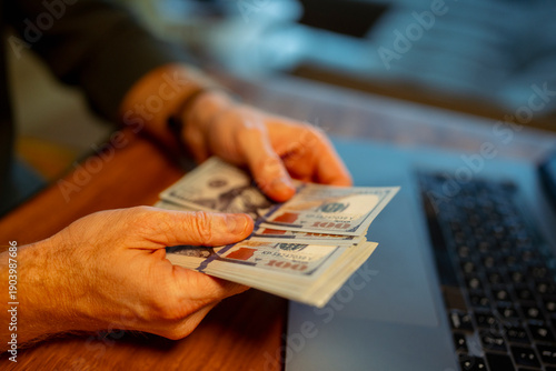 Counting cash at a desk near a laptop during evening
