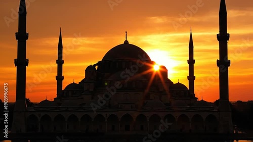 Grand mosque silhouette at sunset with golden sky and water reflection