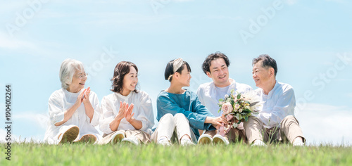 Quadro su tela A park with a view of the blue sky, a family sitting on a hill, parents and chil