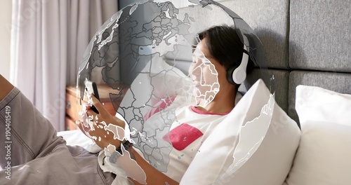 Lying teen wearing white tee red graphic in bedroom, holding phone with headset faint globe overlay
