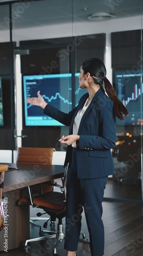 A confident businesswoman leading a presentation in a modern boardroom with large screens showing data charts.