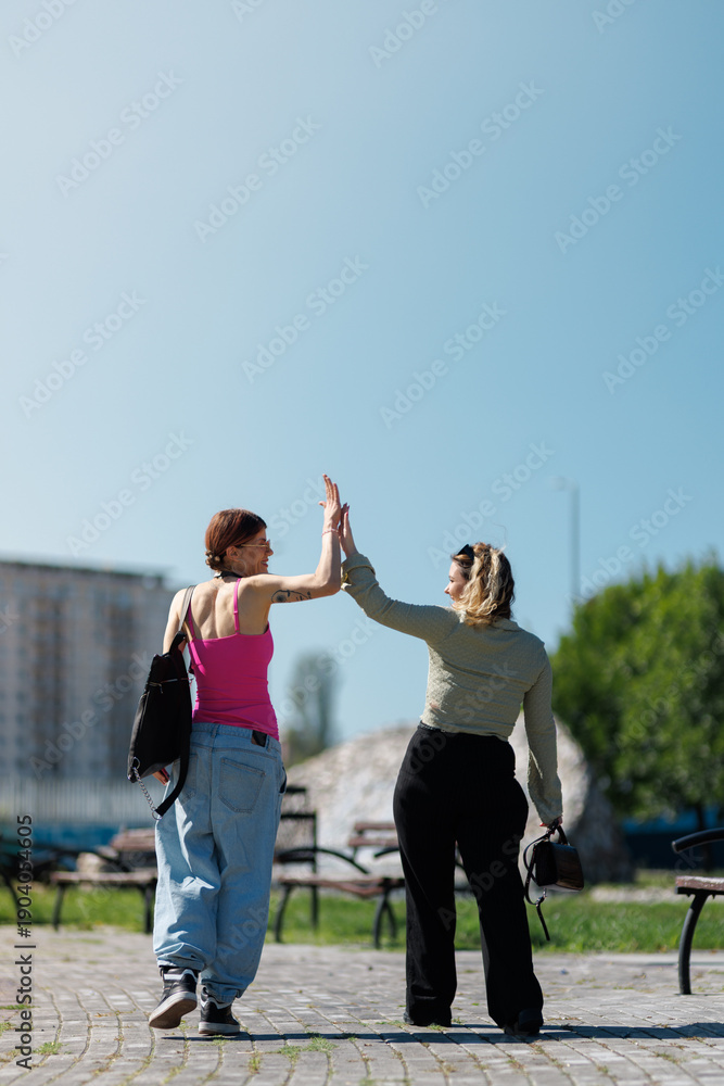 Obraz premium Two women greet each other with a high five in a park on a sunny day while wearing casual clothes and enjoying their time outside