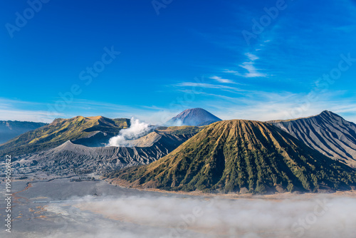 Mount Bromo, an active volcano in east Java, Indonesia as viewed from the rim of the valley. Smoke rising from the crater. Thinning fog on the sandy desert surrounding the mountains. 