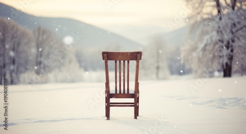 A lone wooden chair stands centered in a snow-covered field, mountains visible in the distance