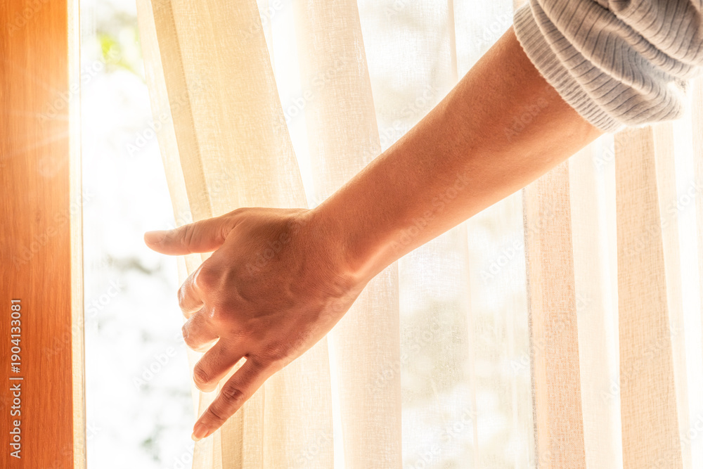 Fototapeta premium woman's hand She opened the curtains on the window. There was morning light through the window in her room, looking at the view of the mountains and trees as the sun rose 