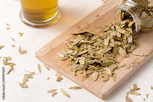 Canvas Print Senna leaves spilling from a mini jar onto wood with tea in the background