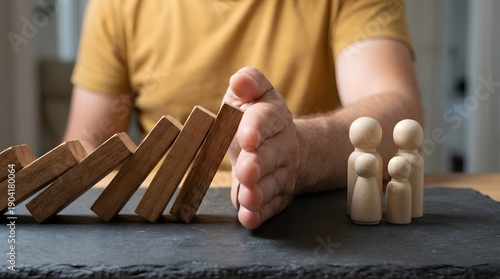 A man's hand stopping falling dominoes from hitting two small human figures, symbolizing protection, safety, and prevention, with a blurred background and a sense of urgency.