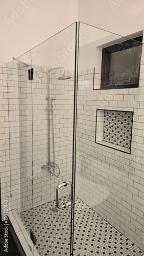Contemporary walk-in shower with frameless glass, chrome rainfall showerhead, white subway tiles and mosaic dot floor. Built-in niche with perforated panel. Clean, bright minimalist bathroom design.