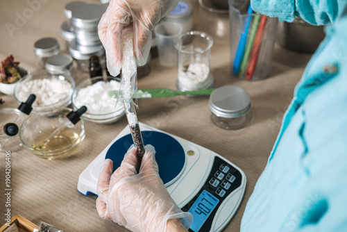 Photos Gloved hands pour white salt crystals into glass test tube to create botanical layers on digital scale
