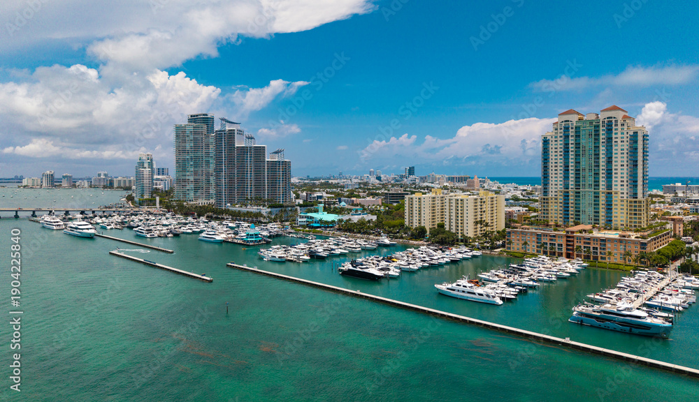 Naklejka premium Luxury yacht docked at Miami marina. Aerial view of coastline in Miami. Sailboat cruising along the Miamis shore. Miami skyline above harbor.