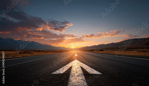Straight asphalt road extending towards the horizon under a vibrant sunset sky with scattered clouds and distant mountain silhouette