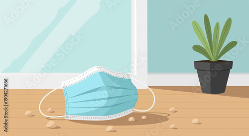 A light blue disposable mask lies on a wooden floor next to a potted plant