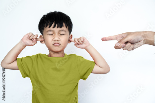 Slika na platnu Stubborn Asian boy covering ears with fingers while being scolded by parent