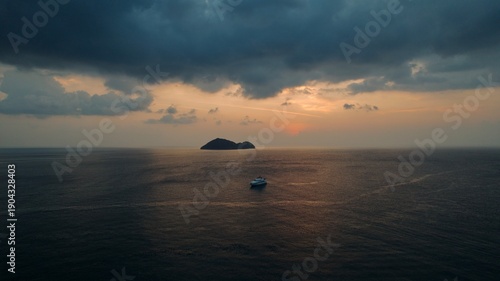 A sunset drone shot over a big boat with an island and blue clouds and dark time. 