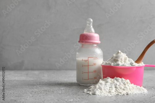 Photos Measuring cup of powdered baby milk formula with bottle on grunge grey backgroun
