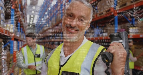 Fotografía Smiling worker wearing hi-vis vest using handheld scanner in warehouse aisle wit