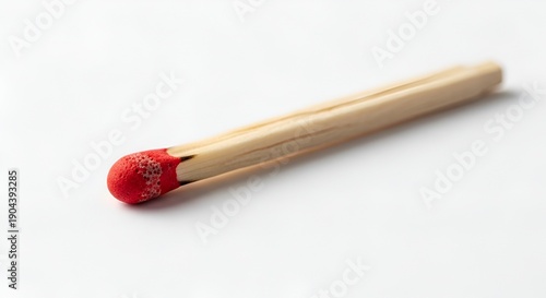 A single matchstick lies on a plain surface viewed from a slight angle