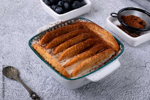 Trendy Japanese yogurt cheesecake with cookies biscuit and blueberries on a gray background. Preparation lazy no bake dessert treat at home