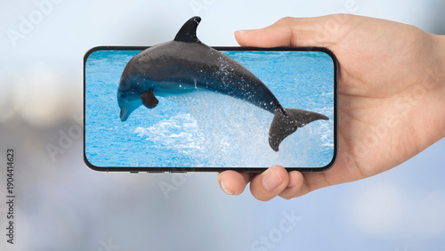 Dolphin Jumping Out of Smartphone Screen Held in Hand Over Ocean Background