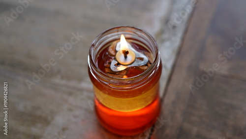 Quadro su tela Burning Candle in a Glass Jar on Wooden Table