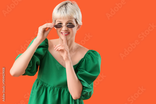 Portrait of beautiful young woman with sunglasses showing silence gesture on ...
