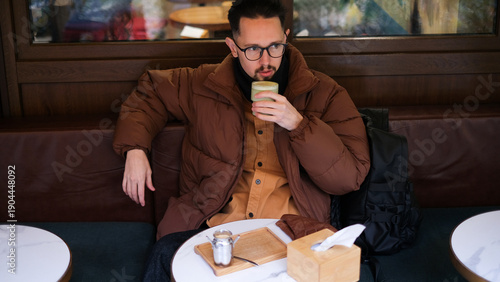  Man in a warm jacket drinking matcha on a cozy cafe terrace on an autumn overcast day