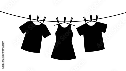 Three dark garments, including two t-shirts and a dress, hang neatly on a clothesline with several clothespins.