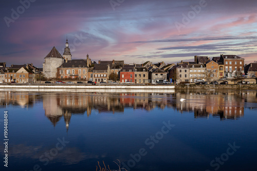 La ville de Givet au coucher du soleil, sur les quais de la Meuse avec le Fort de Charlemont, la tour Victoire et les habitations au bord de l'eau.