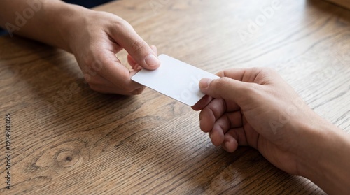 Two hands exchanging a blank white plastic card over a wooden table.